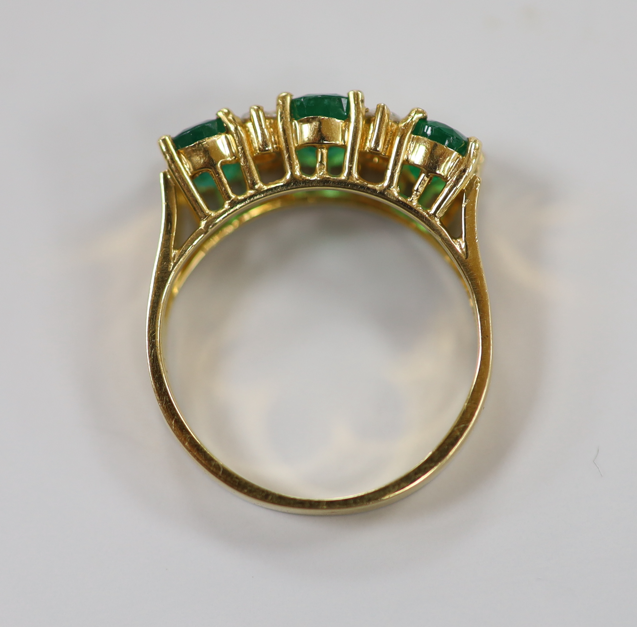 A 750 yellow metal, three stone emerald and four stone diamond spacer set half hoop ring, size K, gross weight 3.8 grams.